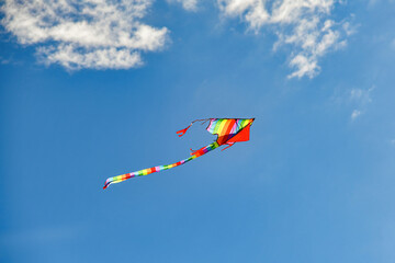 A colorful kite soars among the blue cloudy sky.