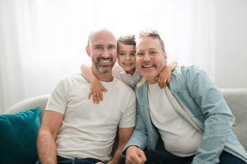 Happy two man couple with adopted child sit on sofa at home