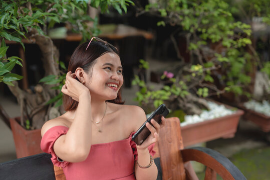 A joyful young lady is smiling widely as she receives a loving message on her smartphone from her boyfriend as she relaxes in sn al fresco coffee shop.