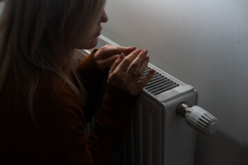 Heating season, woman warms her hands with heater