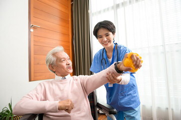 Asian nurse taking care of an elderly man sitting on wheelchair , doing hand exercises at  senior healthcare center.