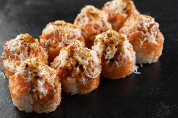 Japanese Baked sushi over black stone background. Tasty and artistic food for restaurant or cafe menu. Rolls on the dish. Japanese cuisine. Sushi menu
