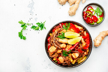 Asian cuisine, stir fry noodles with chicken and vegetables, paprika, zucchini and sesame seeds in bowl. White kitchen table background, top view, space for text