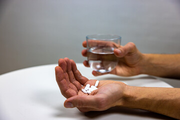A ´photo showing a hand with pills and another hand holding a glass of water. Painkillers....