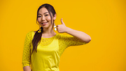 happy asian woman showing thumb up and smiling isolated on yellow