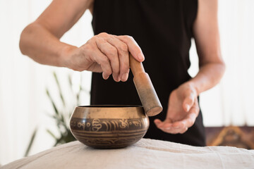 hands using singing bowl in sound healing therapy indoors, closeup
