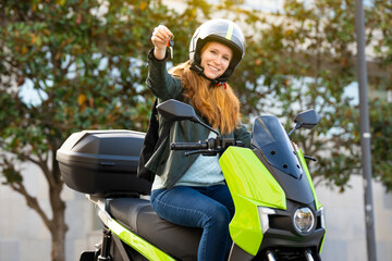 Red-haired woman riding a motorcycle on a city street showing the keys