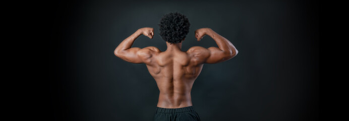 Sportsman showing his back muscles. Athlete flexing muscles. Black background.