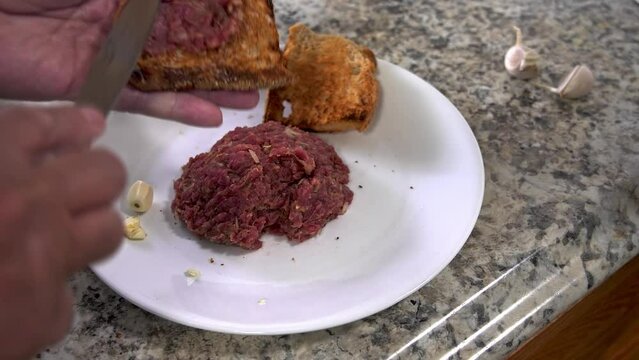 Adding beef steak tartar to toasted bread with garlic