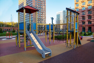 Fototapeta na wymiar Wooden slides made of yellow blue timber on the playground in the courtyard of a residential building against the background of new residential buildings. Playgrounds, sports, health entertainment.