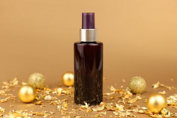 Obraz na płótnie Canvas Brown cosmetic spray bottle, gold Christmas balls, pieces of gold paper on golden background. Body or hair natural oil, skincare, sanitizer, deodorant, moisturizer, micellar water. Mockup, front view