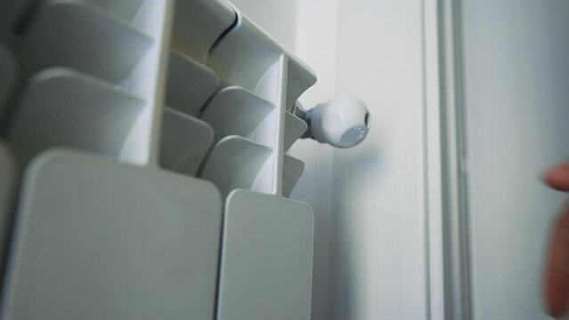 Female hand adjusting thermostat to turn on the radiator heater at home.