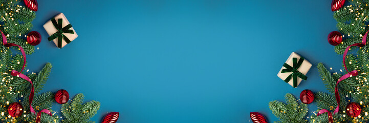 Christmas banner. Gifts wrapped in craft and velvet ribbon, red ornaments and natural green fir tree branches on dark blue background. Holiday template with present. Flat lay, copy space, top view.