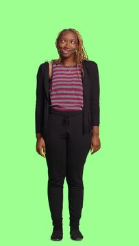 Vertical video: Woman being playful on full body greenscreen backdrop, looking funny or crazy and doing kissy face fooling around. Sticking tongue out acting silly and flirty, joyful girl.