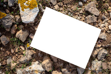 Blank white card with copy space for text or image on a rocky soil texture background. Top view of...