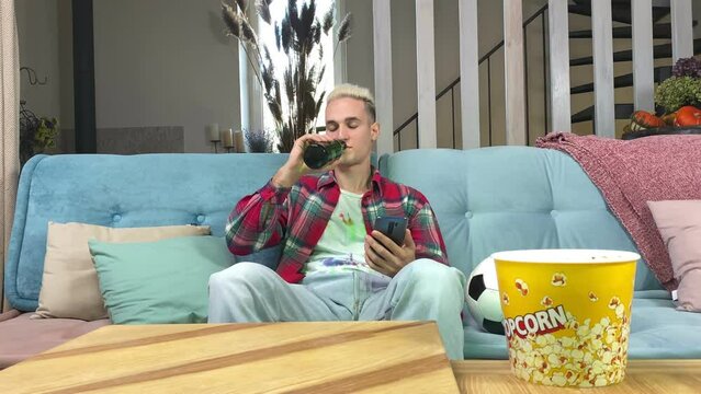 Relaxed young man having profit bet on bookmaker online app, pointing on green chroma key screen indoors. Confident fan making money while watching live sport match on TV sitting on sofa at home.