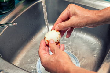 hands peeling a boiled egg under a water jet