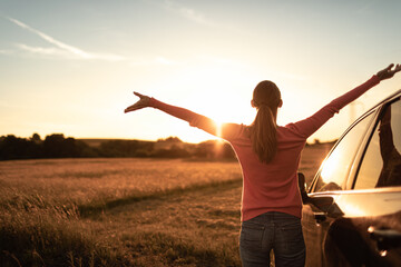 Feeling happy and free in nature. Young female stopping roadside to watching the beautiful sunrise raising arms outstretched to the sky.  - Powered by Adobe