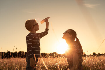little boy using his imagination flying paper airplane in the sky. Mother and child together...