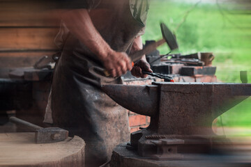 Hands of a man with a hammer on the background of an authentic retro forge. Forging an arrowhead. Added motion blur effect for cinematic look.