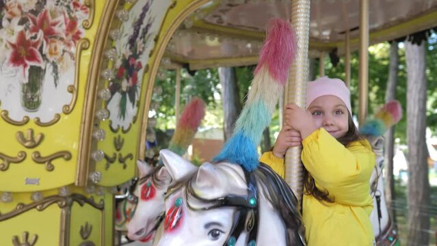 Little cute 5 years old girl ride horse on the old fashioned french carousel. Caucasian girl in warm clothes enjoying and smiling with riding horse on carousel in amusement park on autumn weekend.
