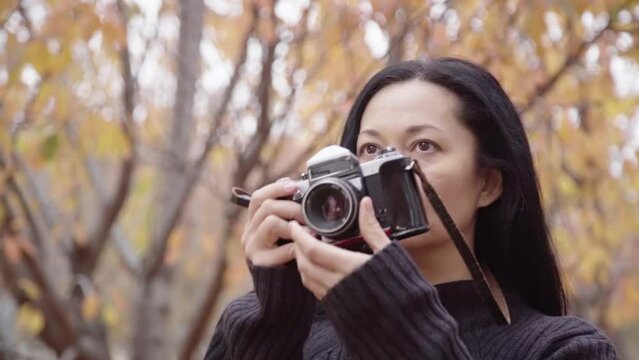 A beautiful girl walks and takes pictures with a film camera in nature, looking up. Autumn season.