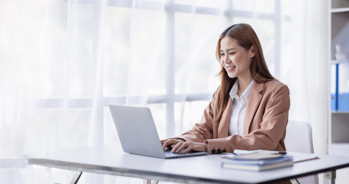 Cheerful Asian female business entrepreneur professional working on laptop while sitting in workplace office desk, business asian woman do Documents, tax, report analysis Savings, finances economy.
