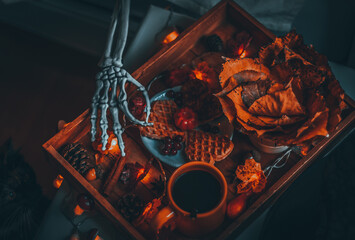 Wooden tray with breakfast and hand skeleton on the bedside table.