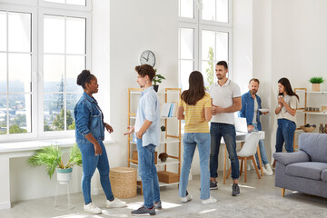 Obraz premium Group of diverse friends meeting and hanging out together. Young multiracial mixed race people in casual clothes standing in room at home, talking to each other, discussing latest events