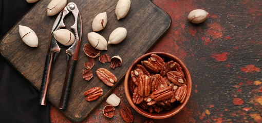Tasty pecan nuts and nutcracker on grunge background, top view