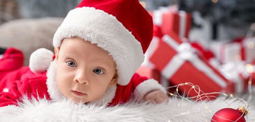 Cute little baby in Santa Claus costume lying on plaid at home on Christmas eve