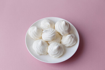 White marshmallows on a white plate on a pink background