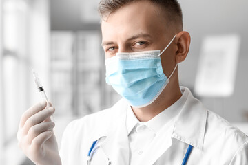 Male doctor in medical mask with syringe at hospital, closeup