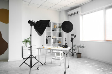 Interior of light office with photographer's workplace, shelving unit and equipment