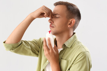 Young man with nosebleed and tissue on white background, closeup