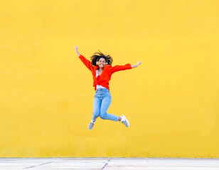 Fototapeta na wymiar Young african american woman with headphones jumping for joy over a yellow wall