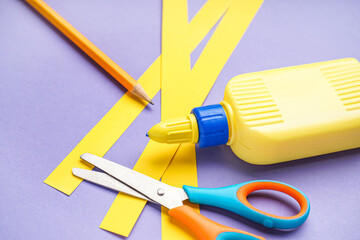 Bottle of glue, paper stripes, pencil and scissors on color background, closeup