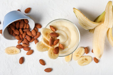 Glass of tasty vanilla pudding with banana and almond nuts on light background
