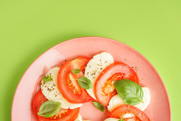 Plate of tasty caprese salad on green background, closeup