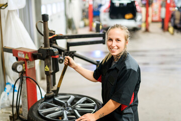 Fototapeta na wymiar Nice and cool mechanic woman changing car tire at work