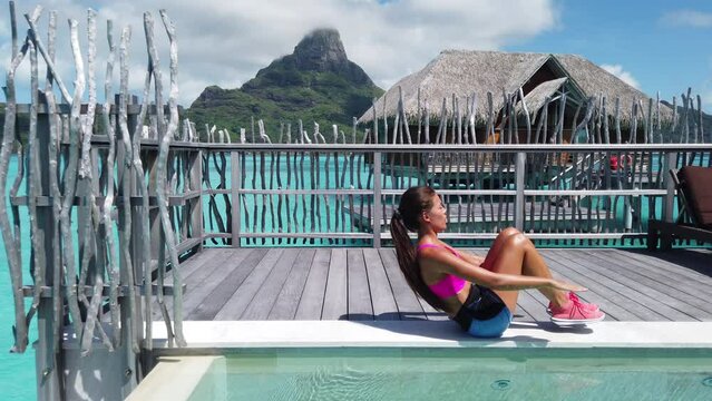 Active Travel. Fitness woman toned with in shape body doing V-up Crunch ab toning exercise workout as part of an active lifestyle. Bodyweight exercises on Bora Bora travel vacation