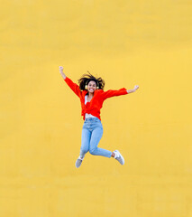 Young african american woman with headphones jumping for joy over a yellow wall