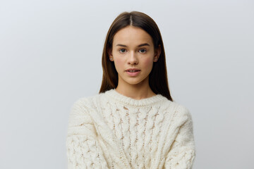 a young, beautiful, sophisticated woman stands in a warm white knitted sweater on a light...