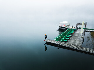 Young woman standing alone on footbridge and staring at lake. Mist over water. Foggy air. Chilly morning. Empty place for sentimental, inspirational text, quote or sayings. Aerial view