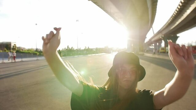 Expressive young woman with long straight hair dancing under the bridge in bright sunlight