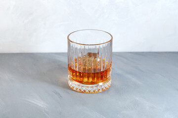 Whiskey on the rocks or scotch with ice cubes in Old fashion glass. Grey background, selective...