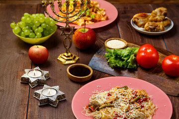 Traditional Jewish dishes on the set table, fruits, burning candles and menorah.