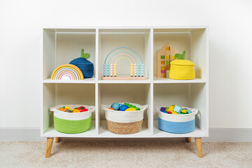 Colorful storage baskets on shelves. White shelving with rainbow wooden toys in cloth stylish...