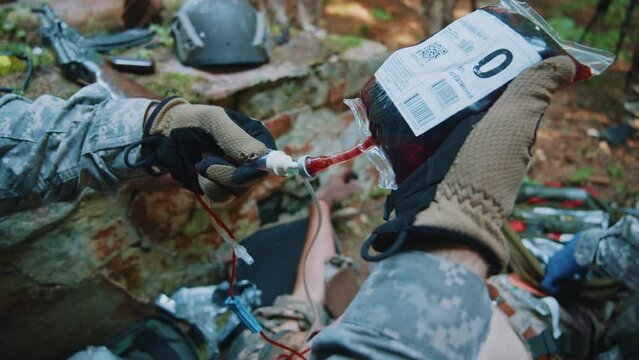Combat medic provides first aid to a soldier wounded. Preparing to receiving blood transfusion. War. Military concept