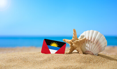 Tropical beach with seashells and Antigua and Barbuda flag. The concept of a paradise vacation on...